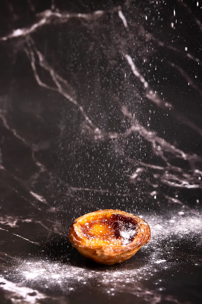 Pastel de nata artesanal da Pastelaria Patyanne sobre fundo escuro com açúcar em pó