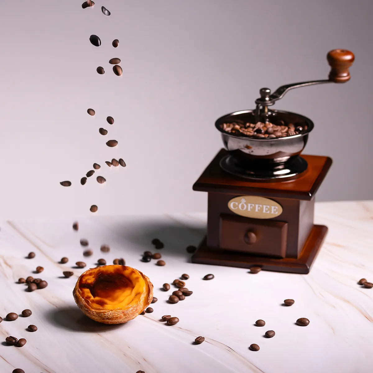 Pastel de nata artesanal da Pastelaria Patyanne com moinho de café e grãos sobre fundo claro
